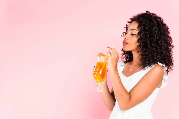 Африканская американская девушка смотрит на стакан с коктейлем на розовом — стоковое фото