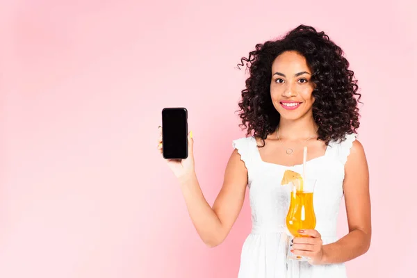 Allegra ragazza afroamericana con smartphone in mano con schermo bianco e cocktail su rosa — Foto stock