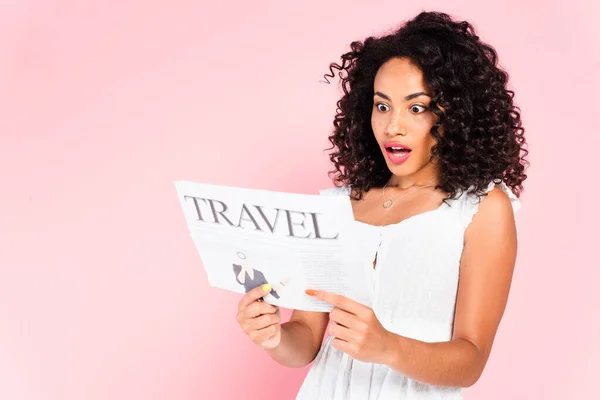 Chica afroamericana sorprendida leyendo periódico de viaje aislado en rosa - foto de stock