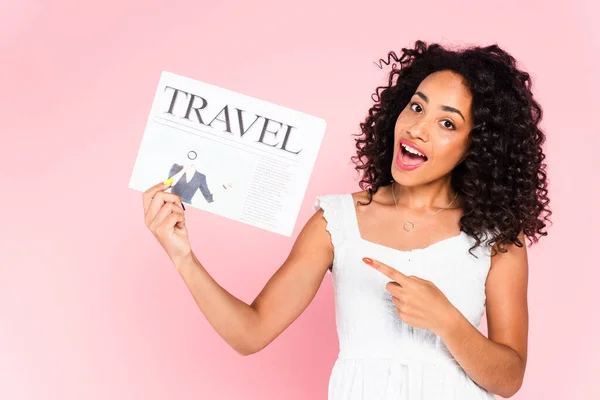 Encaracolado afro-americano mulher apontando com o dedo para jornal de viagem isolado em rosa — Fotografia de Stock