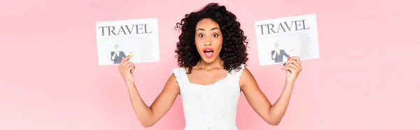 Horizontal crop of shocked african american woman holding travel newspapers isolated on pink — Stock Photo