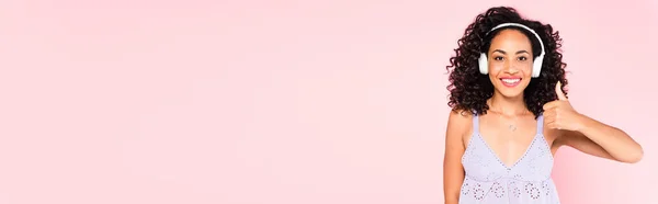 Raccolto panoramico di felice ragazza afroamericana in cuffie wireless ascoltare musica e mostrando pollice in su isolato su rosa — Foto stock