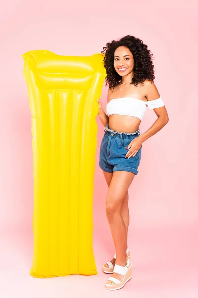 Happy african american girl standing near inflatable mattress on pink — Stock Photo