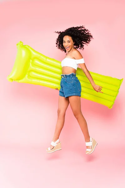 Chica americana africana feliz que salta con el colchón inflable en rosa - foto de stock