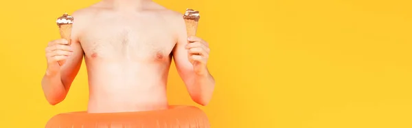 Panoramic crop of shirtless man holding ice cream cones isolated on yellow — Stock Photo