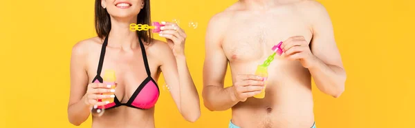 Récolte panoramique de fille heureuse en maillot de bain près de l'homme torse nu et bulles de savon isolé sur jaune — Photo de stock