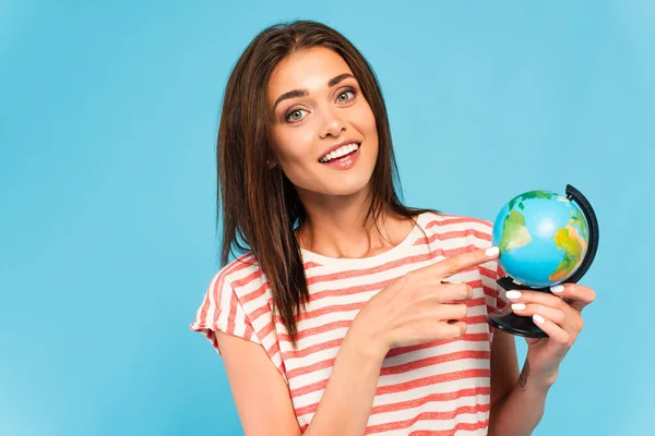 Щаслива дівчина вказує пальцем на глобус ізольовано на синьому — стокове фото
