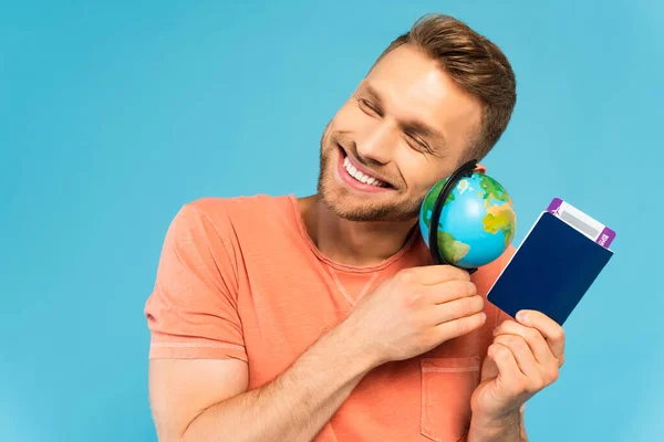 Щасливий бородатий чоловік із закритими очима тримає паспорт і глобус ізольовані на синьому — стокове фото