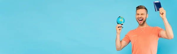 Панорамная концепция взволнованного бородатого человека с закрытыми глазами, держащего паспорт и глобус изолированным на голубом — стоковое фото