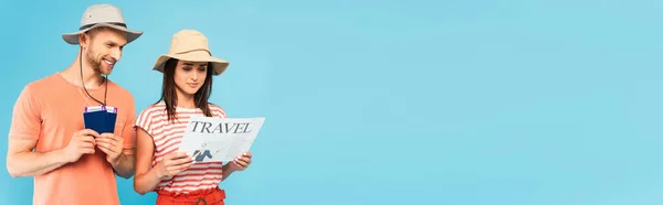 Panoramic shot of girl in hat reading travel newspaper near man holding passports isolated on blue — Stock Photo