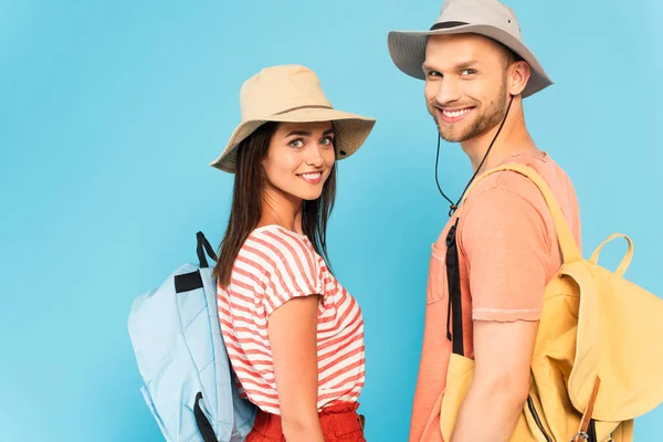 Happy couple in hats with backpacks looking at camera isolated on blue — Stock Photo