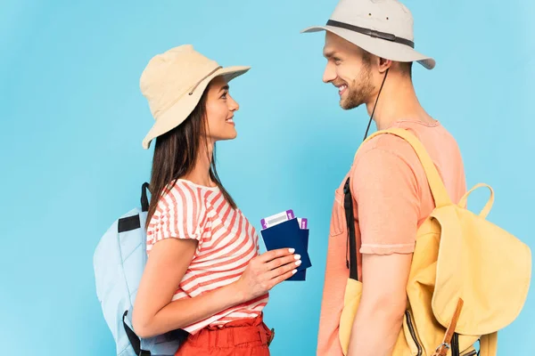 Vista laterale di donna felice in cappello in possesso di passaporti vicino allegro fidanzato isolato su blu — Foto stock