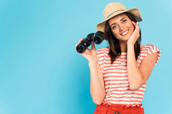 Молодая счастливая женщина в шляпе держит бинокль на голубом — стоковое фото