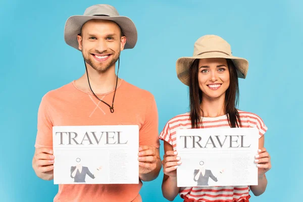 Happy couple in hats holding travel newspapers isolated on blue — Stock Photo