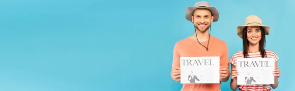 Panoramic concept of happy couple in hats holding travel newspapers isolated on blue — Stock Photo