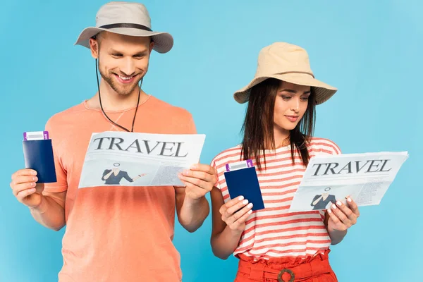 Glückliches Paar mit Hut, das Reisezeitungen liest und Reisepässe isoliert auf blauem Grund hält — Stockfoto