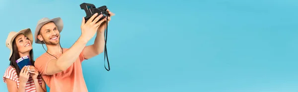 Panoramic shot of happy man in hat holding vintage camera and taking selfie with cheerful girl isolated on blue — Stock Photo