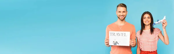 Conceito panorâmico de mulher feliz segurando avião de brinquedo perto de homem barbudo com jornal de viagem isolado em azul — Fotografia de Stock