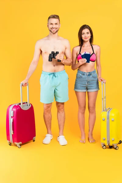 Couple heureux avec jumelles et passeports debout près des bagages sur jaune — Photo de stock