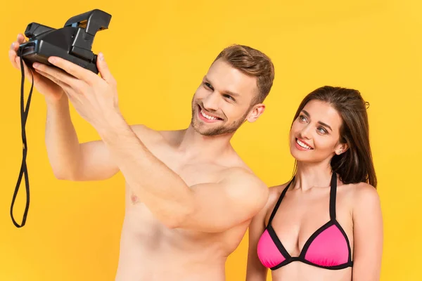 Happy shirtless man taking selfie with girlfriend on vintage camera isolated on yellow — Stock Photo