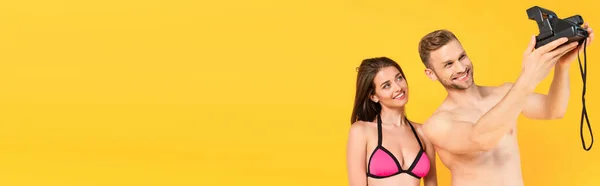 Horizontal image of happy shirtless man taking selfie with girlfriend on vintage camera isolated on yellow — Stock Photo