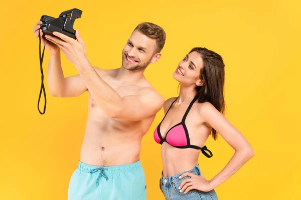 Happy shirtless man taking selfie with woman on vintage camera isolated on yellow — Stock Photo