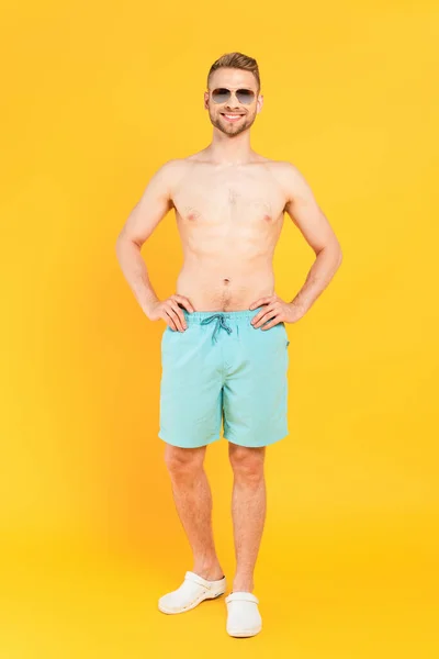 Hombre feliz sin camisa en gafas de sol de pie con las manos en las caderas en amarillo - foto de stock