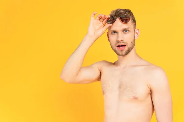 Uomo scioccato e senza camicia toccando occhiali da sole isolati su giallo — Foto stock