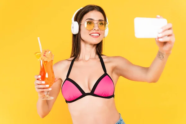 Selective focus of cheerful and tattooed girl in sunglasses taking selfie while holding cocktail isolated on yellow — Stock Photo