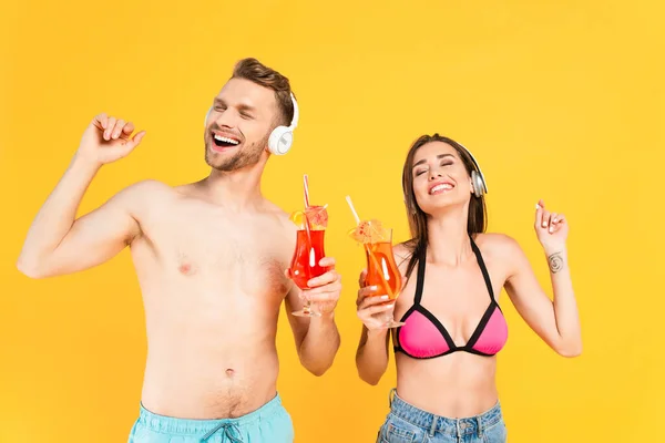 Happy man and woman in headphones holding cocktails isolated on yellow — Stock Photo