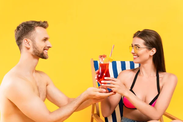 Barbudo hombre celebración cóctel cerca atractiva y feliz chica en gafas de sol aislado en amarillo - foto de stock