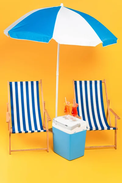 Deck chair near beach umbrella and cocktails on portable fridge freezer on yellow — Stock Photo