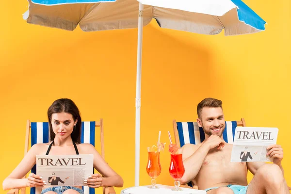 Feliz pareja leyendo periódicos de viaje y sentado en tumbonas en amarillo - foto de stock