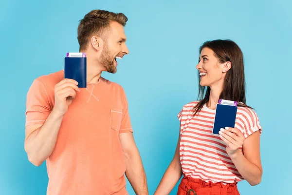 Couple heureux détenant des passeports avec des billets d'avion et se regardant isolé sur bleu — Photo de stock