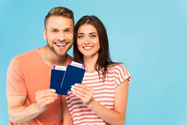 Feliz pareja sosteniendo pasaportes con billetes de avión aislados en azul - foto de stock