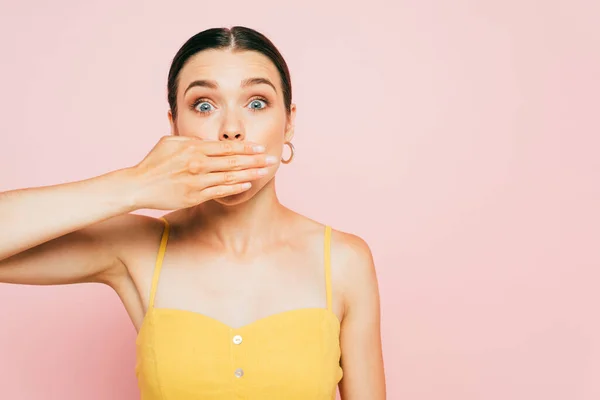 Shocked brunette young woman covering mouth with hand isolated on pink — Stock Photo