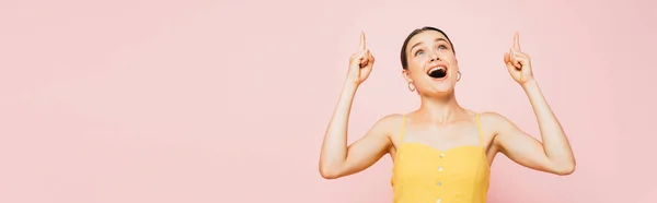 Excitada morena joven apuntando con los dedos hacia arriba aislado en rosa, tiro panorámico - foto de stock