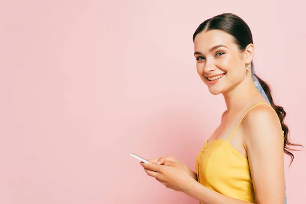 Вид сбоку молодой брюнетки, использующей смартфон, изолированный на розовом фоне — стоковое фото