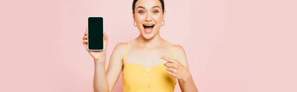 Excited brunette woman holding smartphone with blank screen isolated on pink, panoramic shot — Stock Photo