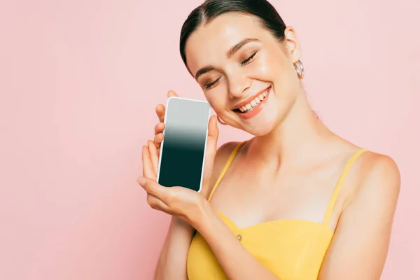 Брюнетка молода жінка тримає смартфон з порожнім екраном ізольовано на рожевому — стокове фото