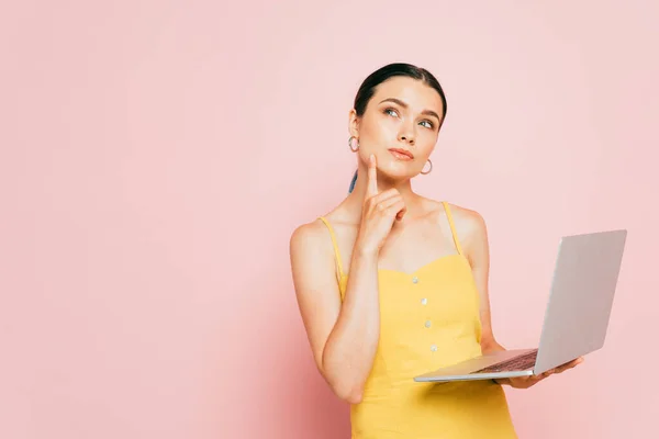 Morena pensativa joven usando el ordenador portátil en rosa - foto de stock