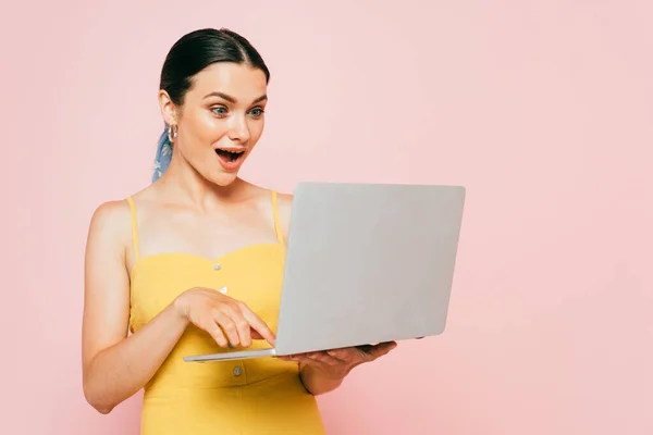 Surprised brunette young woman using laptop isolated on pink — Stock Photo