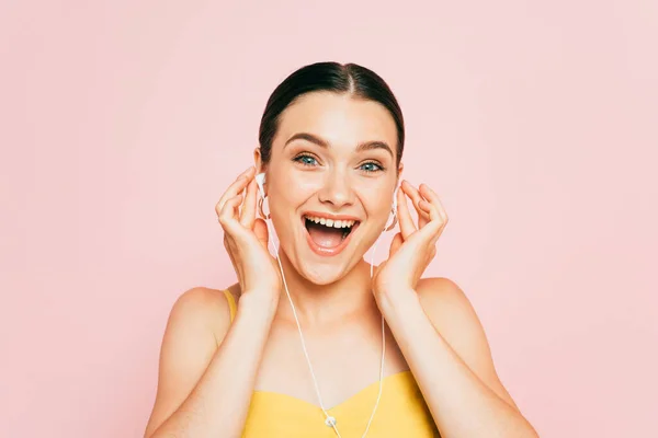 Aufgeregte brünette junge Frau hört Musik in Kopfhörern isoliert auf rosa — Stockfoto