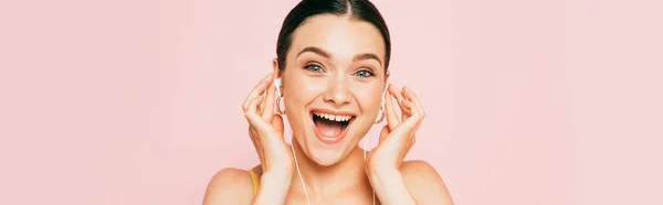 Збуджена брюнетка молода жінка слухає музику в навушниках ізольовано на рожевому, панорамному кадрі — стокове фото