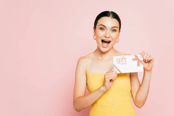 Excited brunette young woman holding gift card isolated on pink — Stock Photo