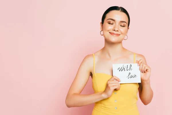 Brünette junge Frau mit geschlossenen Augen mit Liebeskarte auf rosa — Stockfoto