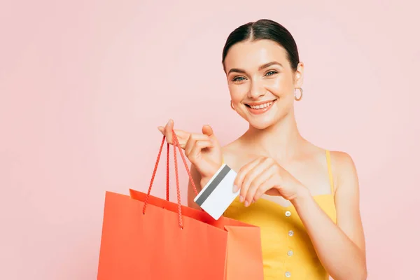 Брюнетка молода жінка кладе кредитну картку в сумку для покупок ізольовано на рожевому — стокове фото