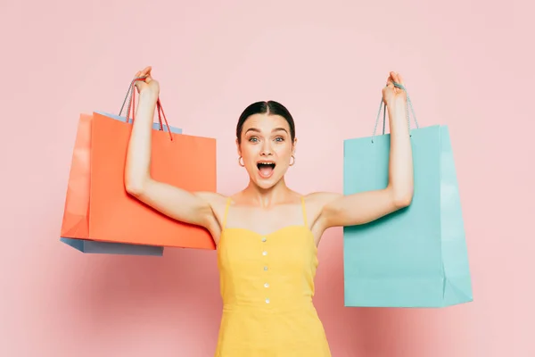 Excited brunette young woman with shopping bags in raised hands on pink — Stock Photo