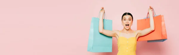 Excited brunette young woman with shopping bags in raised hands on pink, panoramic shot — Stock Photo