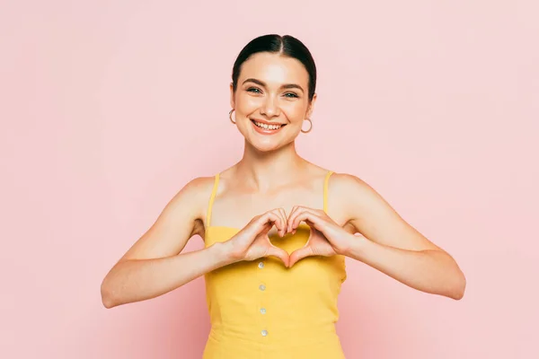 Brunette young woman showing heart gesture isolated on pink — Stock Photo